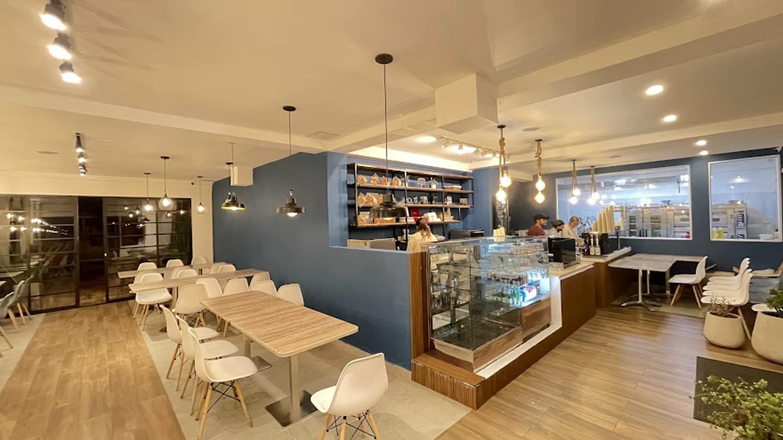 Salón de Balenzia: mesa comunal de madera, sillas blancas y la barra con la vitrina de pan